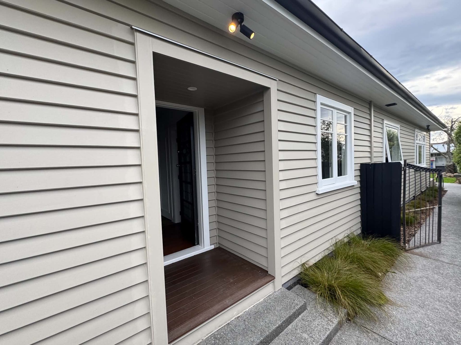 Grey weatherboard entrance with white trim and native planting